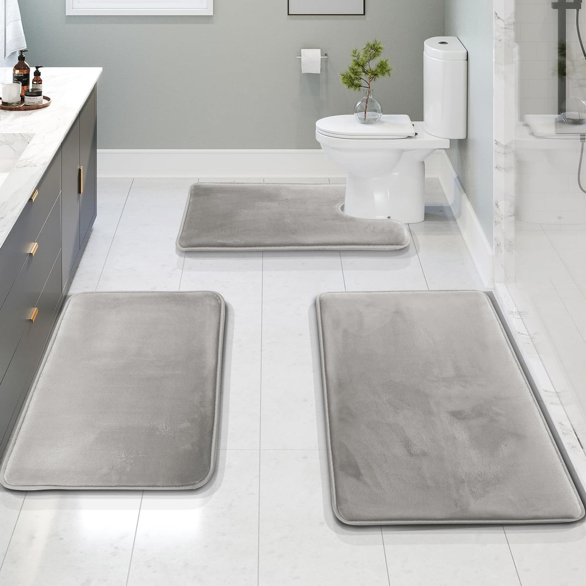Gray bath mats on a bathroom floor with a toilet and sink in the background.