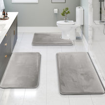 Gray bath mats on a bathroom floor with a toilet and sink in the background.