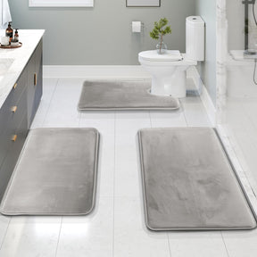 Gray bath mats on a bathroom floor with a toilet and sink in the background.