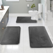 Three gray bath mats on a bathroom floor with a toilet and sink in the background.