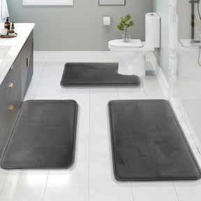 Three gray bath mats on a bathroom floor with a toilet and sink in the background.