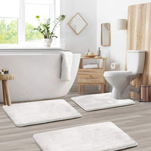 Bathroom with white bath mats on wooden floor, toilet, and bathtub.