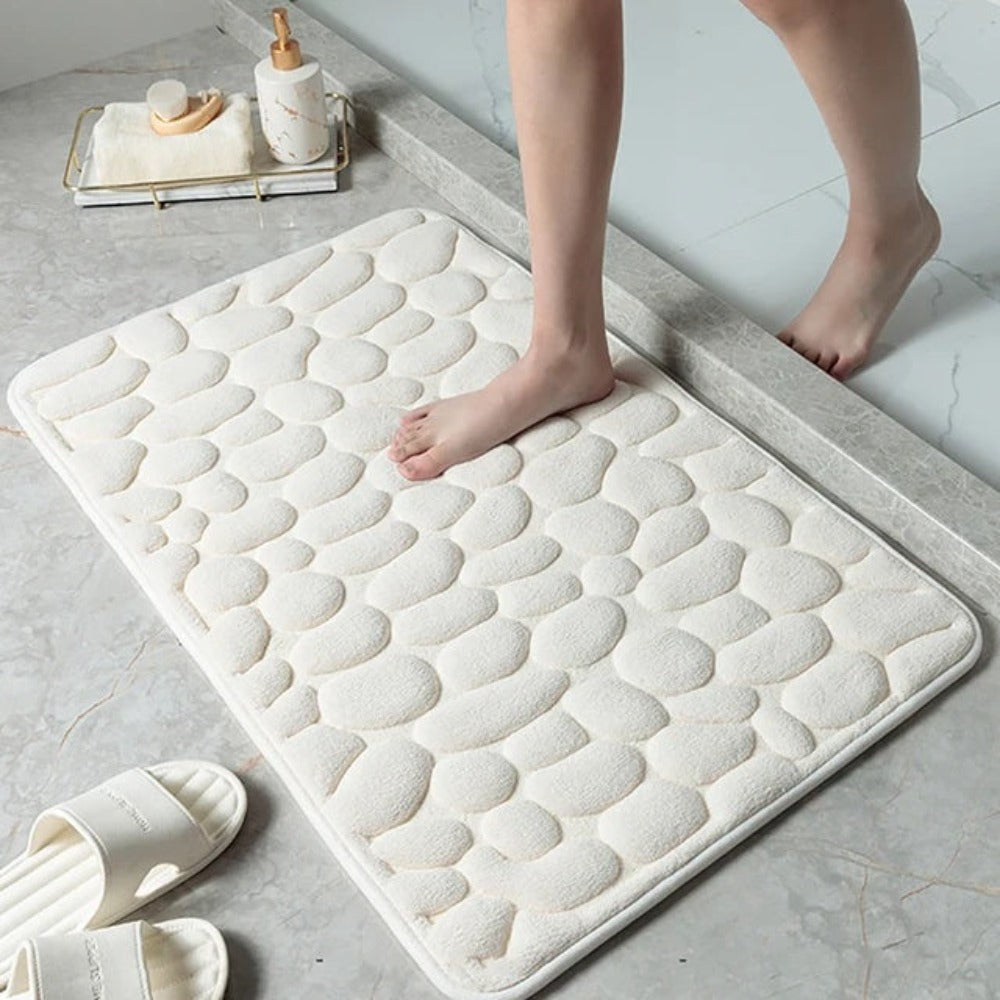 White textured bath mat on a bathroom floor with a person stepping onto it.