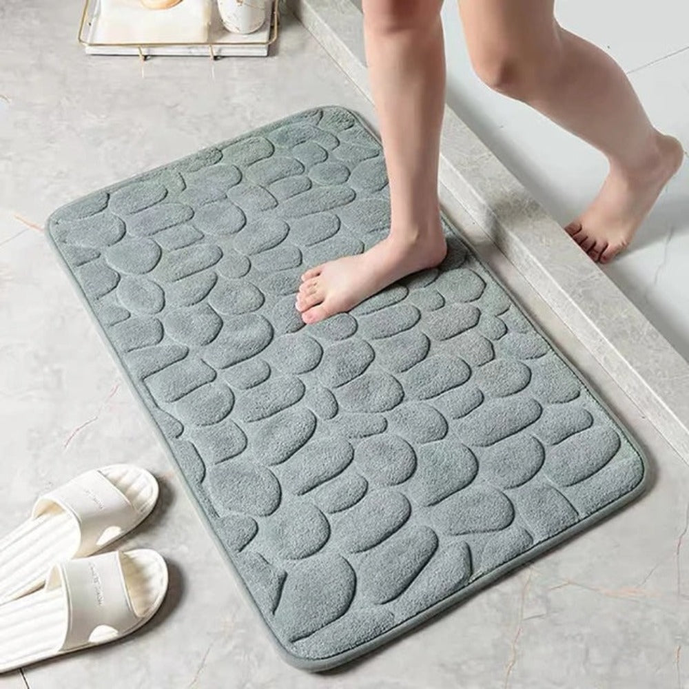 Gray textured bath mat on a bathroom floor with a person stepping onto it.