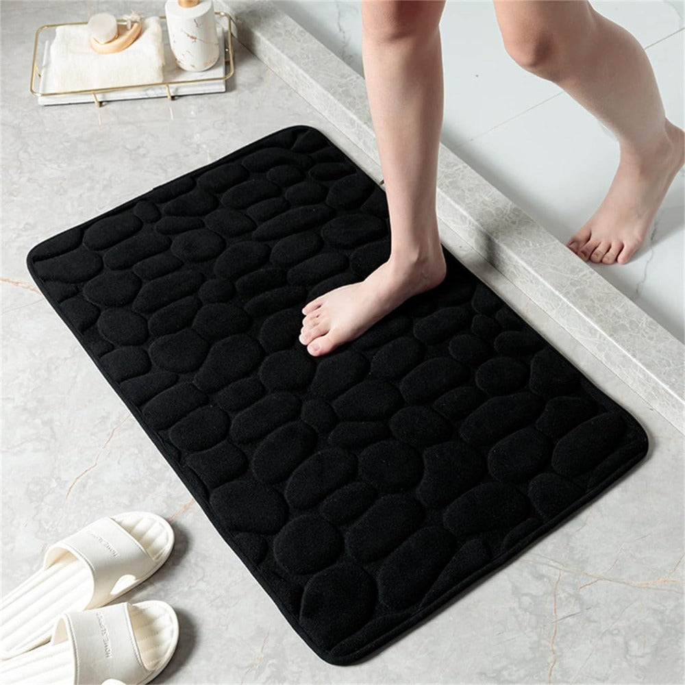 Person stepping onto a black textured bath mat in a bathroom setting.
