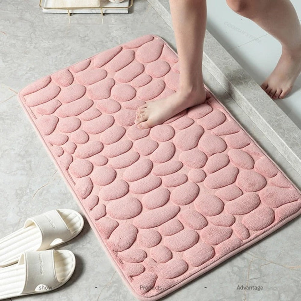 Pink textured bath mat on a bathroom floor with a child's feet stepping onto it.