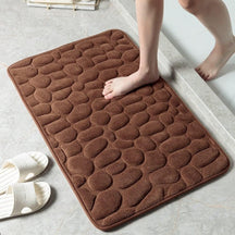 Brown textured bath mat on a bathroom floor with a person stepping onto it.