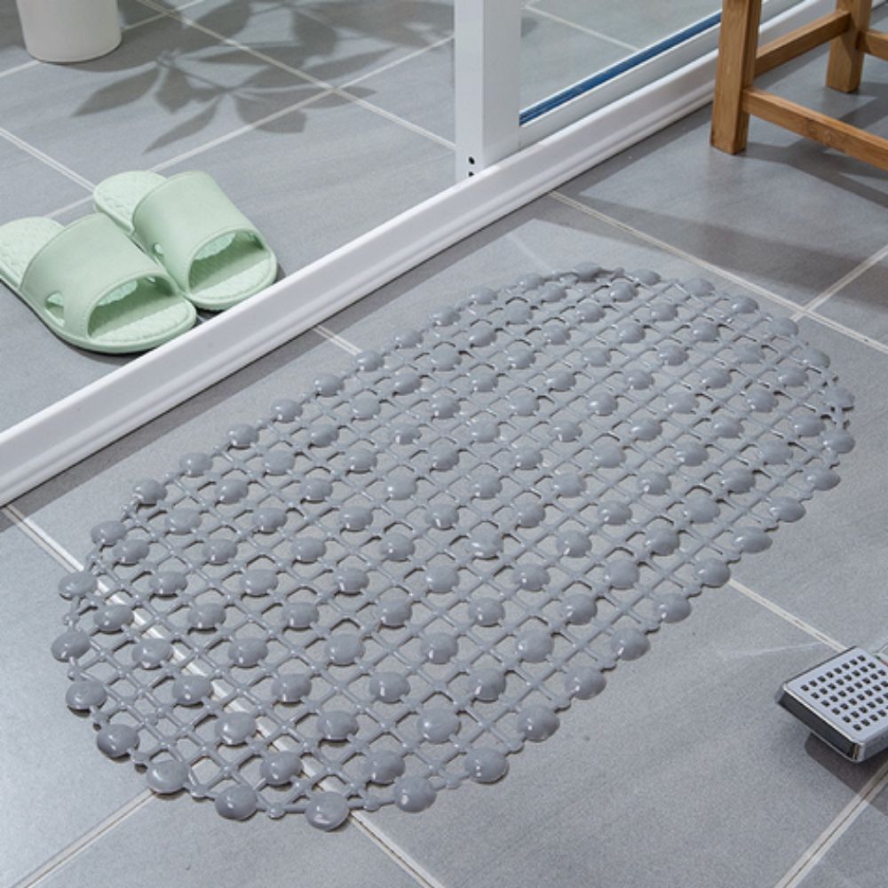 Gray textured bath mat on a tiled bathroom floor with green slippers nearby.