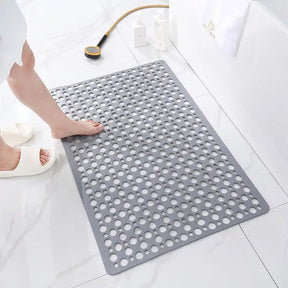 Gray textured bath mat on a white tiled bathroom floor with a person stepping onto it.
