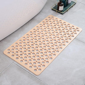 Beige bath mat with circular holes on a bathroom floor.