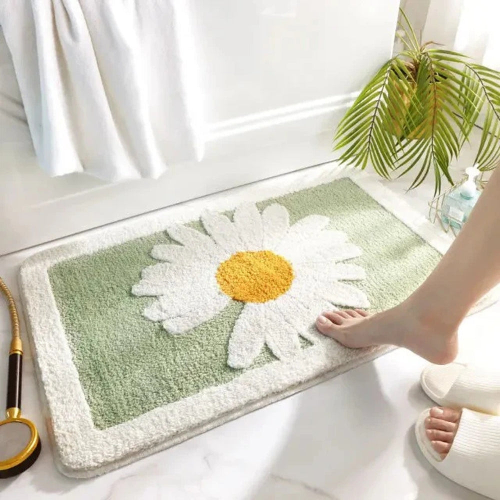 Person stepping onto a green bath mat with a white flower design on a light wooden floor.