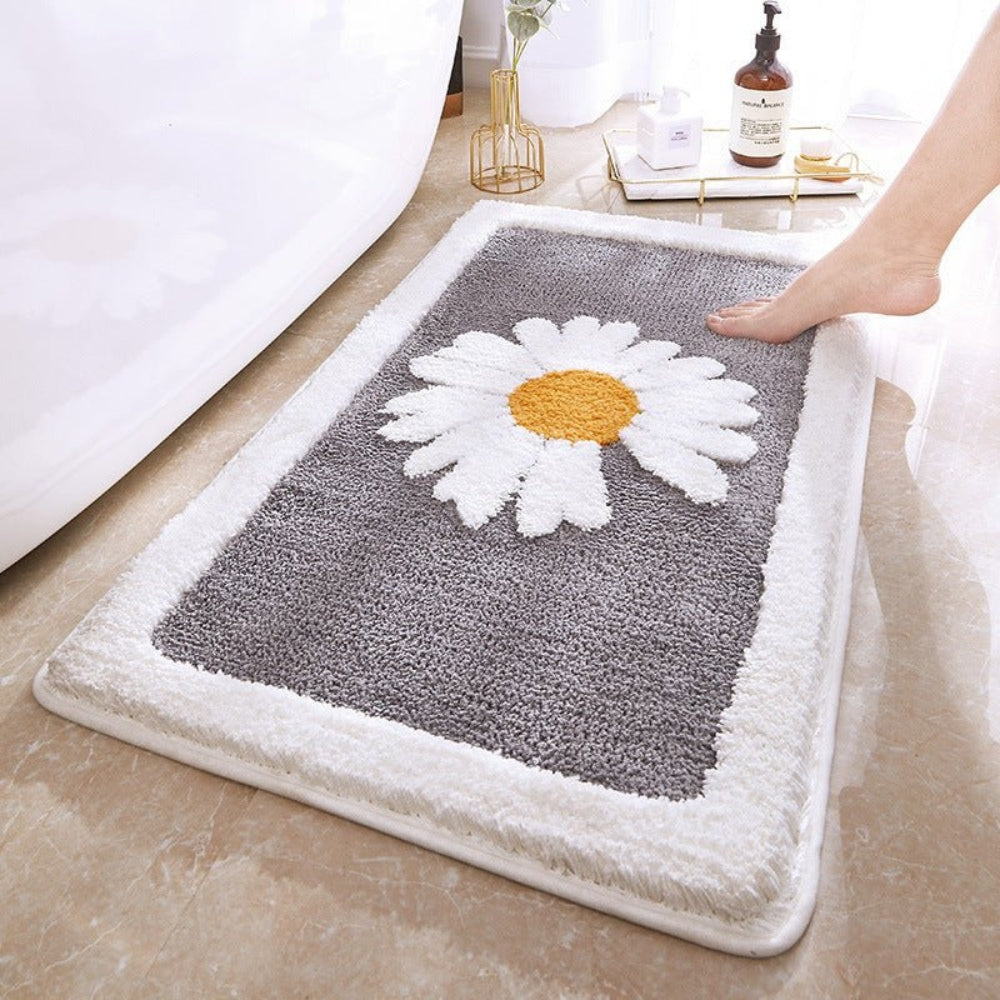 Gray bath mat with a white daisy design on a bathroom floor.