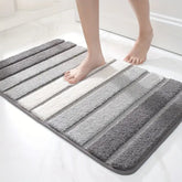 Striped bath mat with gray, white, and black stripes on a white floor.