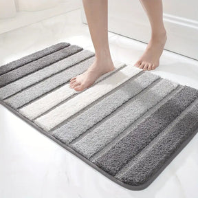 Striped bath mat with gray, white, and black stripes on a white floor.