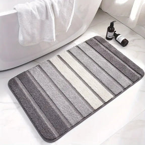 Striped bath mat on a bathroom floor with a bathtub and bottles in the background.