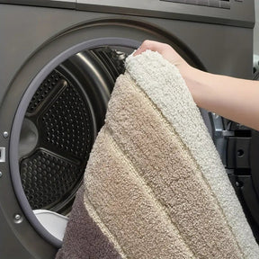 Person holding a textured towel in front of an open washing machine.