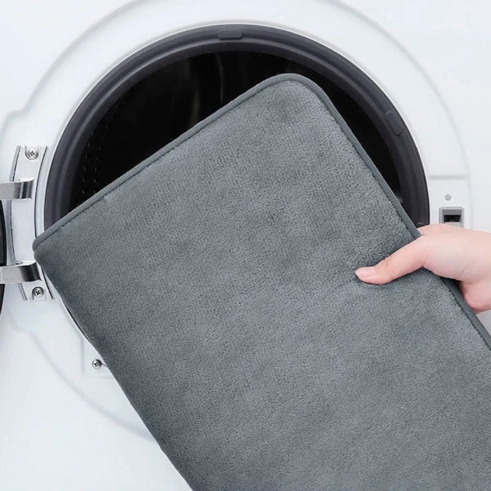 Person holding a gray mat in front of an open washing machine.