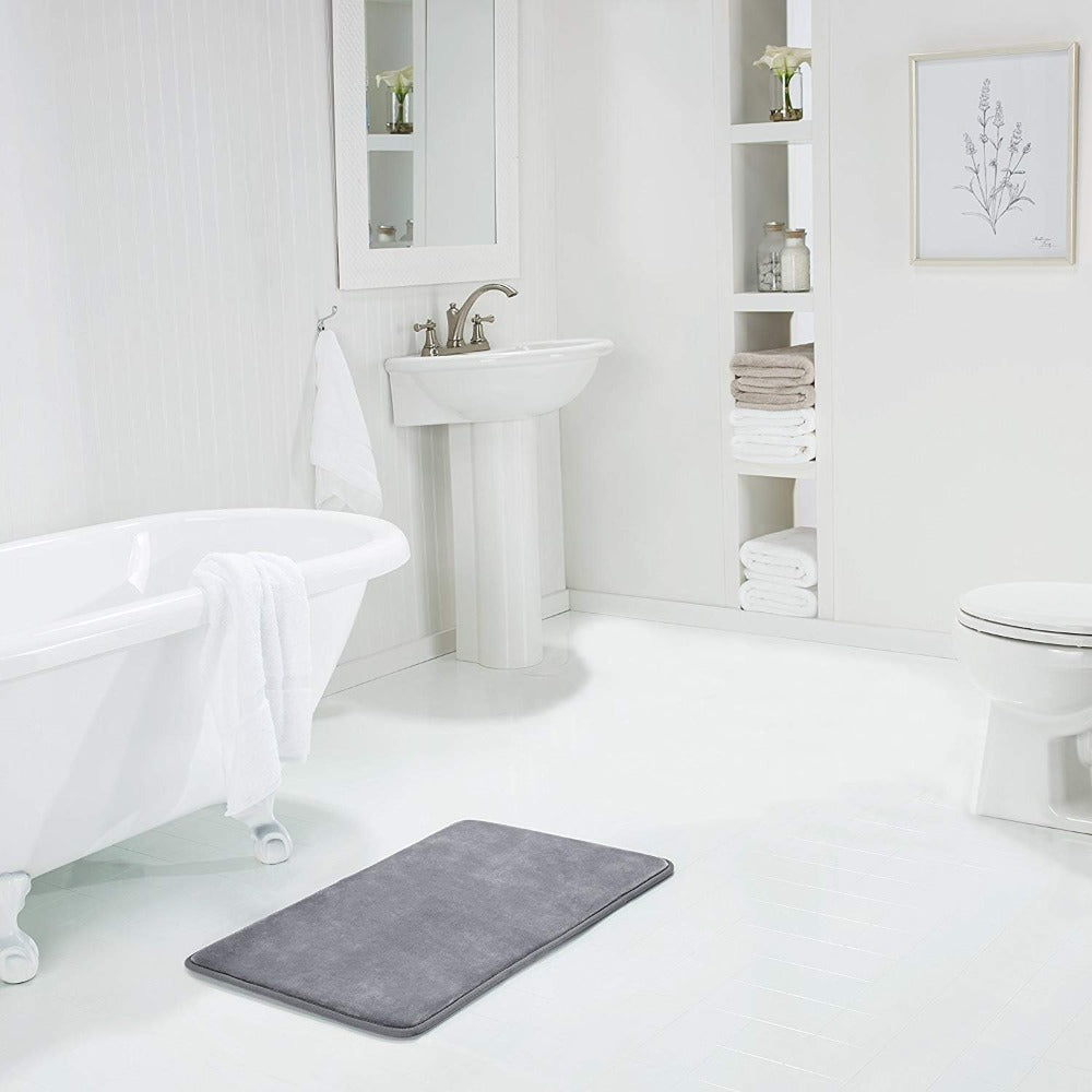 Gray bath mat on a white bathroom floor with a bathtub, sink, and toilet in the background.