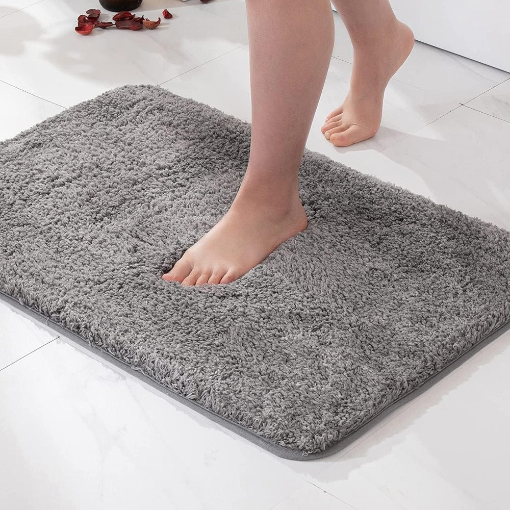 Person stepping onto a gray bath mat on a white tiled floor