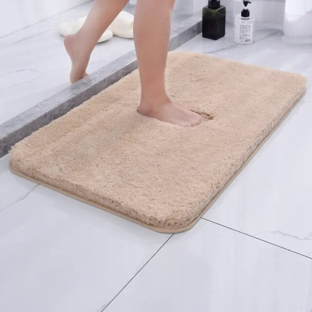 Beige bath mat on a bathroom floor with a person stepping onto it.