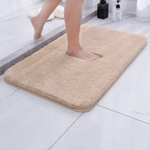 Beige bath mat on a bathroom floor with a person stepping onto it.