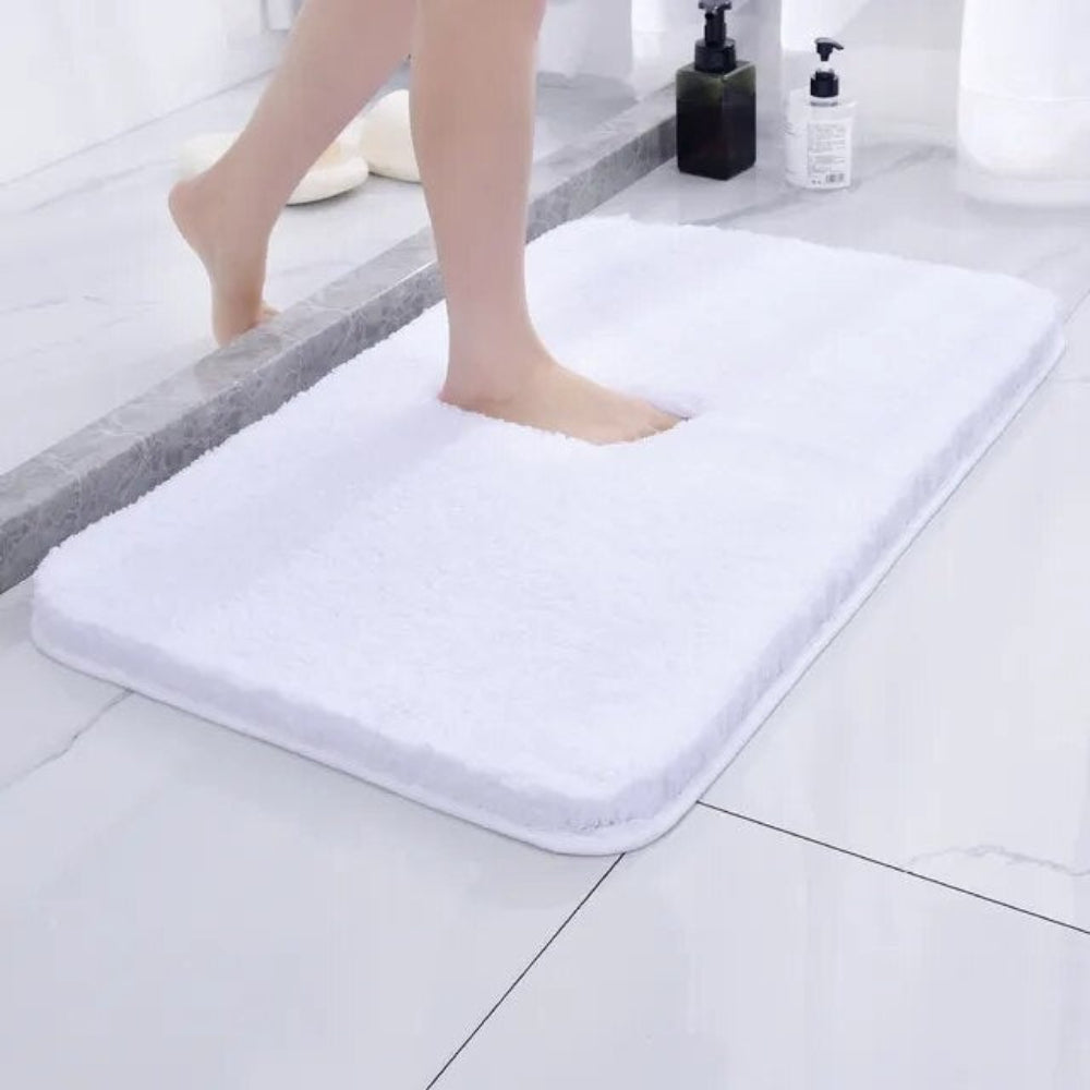 White bath mat on a bathroom floor with a person stepping onto it.