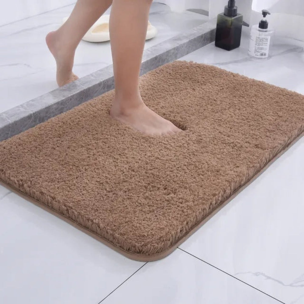 Brown bath mat on a bathroom floor with a foot stepping onto it.