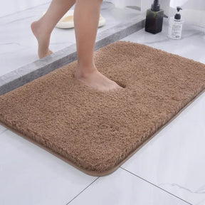 Brown bath mat on a bathroom floor with a foot stepping onto it.