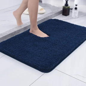 Navy blue bath mat on a bathroom floor with a person stepping onto it.