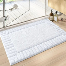 White bath mat on a wooden floor with a glass shower door in the background