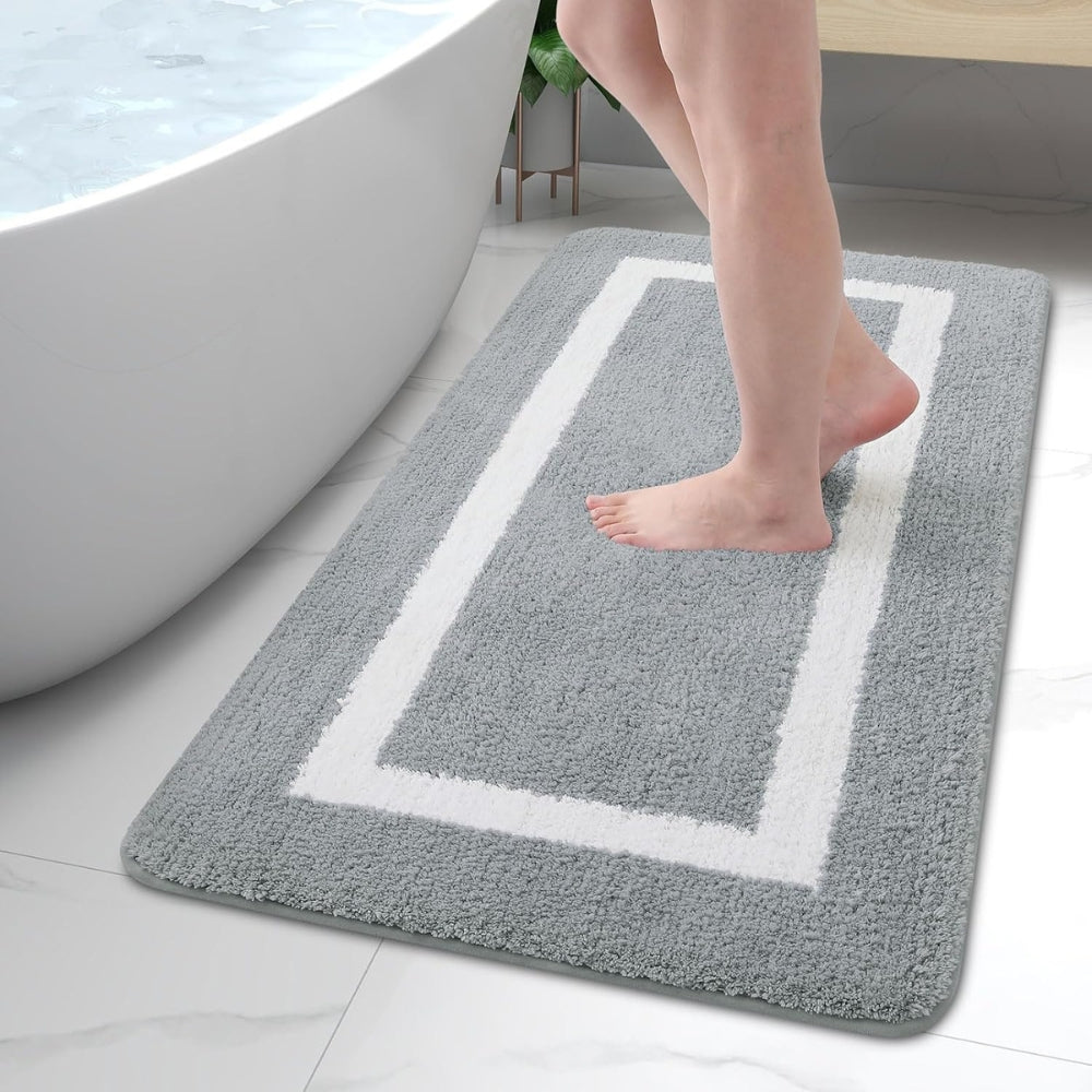 Person stepping onto a gray bath mat with a white border near a bathtub.