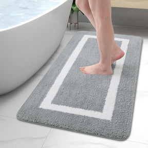 Person stepping onto a gray bath mat with a white border near a bathtub.