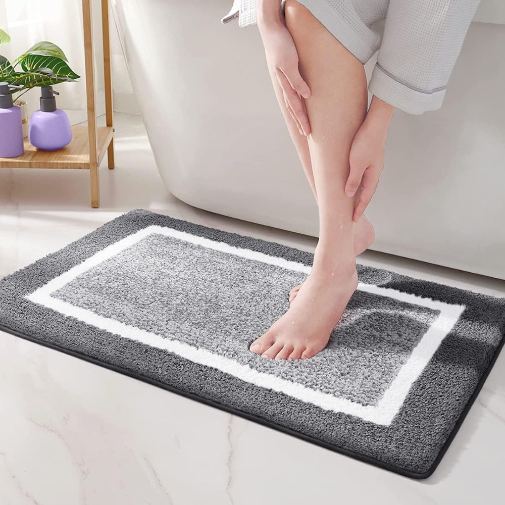 Person stepping onto a gray bath mat with a white border in a bathroom setting.