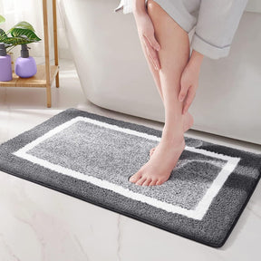 Person stepping onto a gray bath mat with a white border in a bathroom setting.