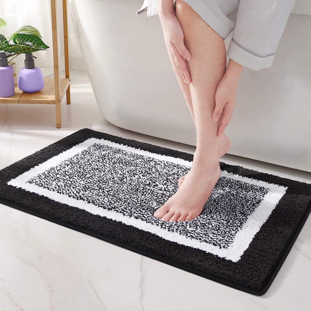 Person stepping onto a black and white patterned bath mat in a bathroom setting.