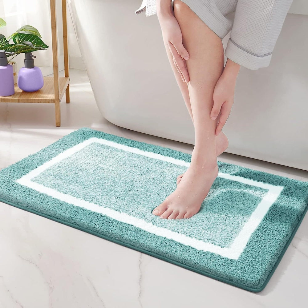 Person stepping onto a teal bath mat with a white border in a bathroom setting.
