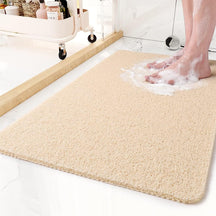 Beige bath mat on a bathroom floor with soapy water and feet stepping onto it.