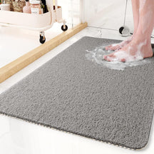 Gray bath mat with soapy water and feet on a bathroom floor.