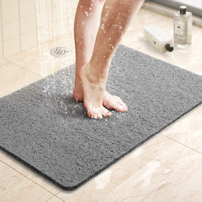 Person stepping onto a gray bath mat in a bathroom setting.
