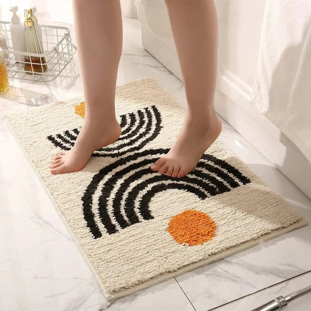 Person stepping onto a bath mat with black and orange design on a bathroom floor.