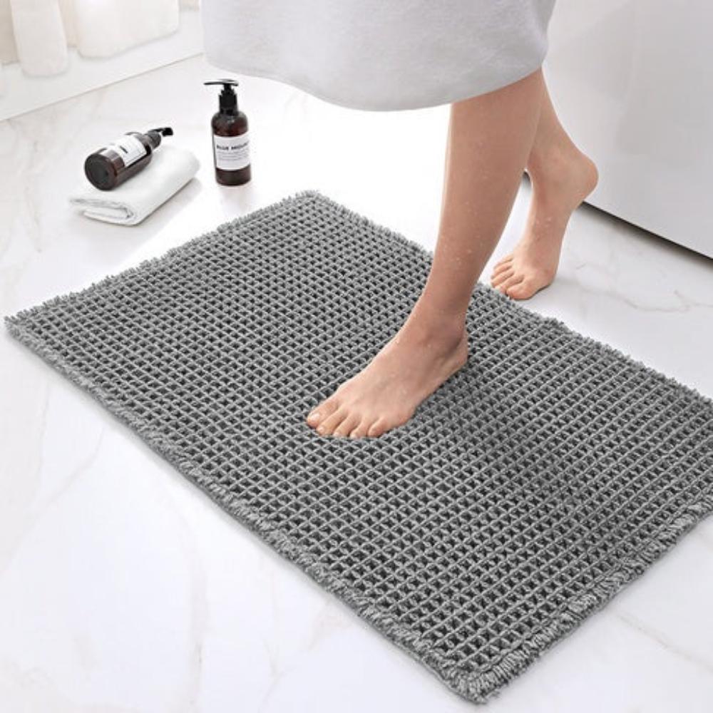 Person stepping onto a gray bath mat with bathroom items in the background