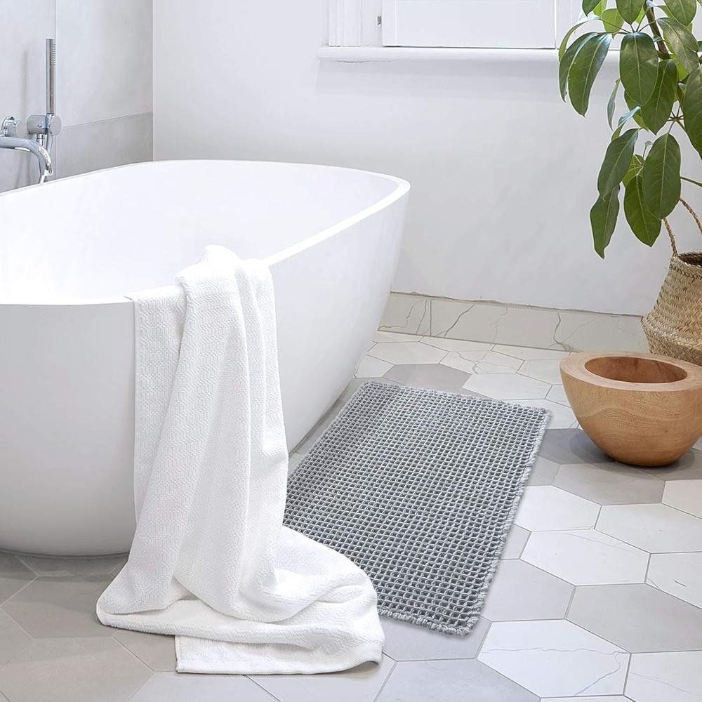 Bathroom with a white bathtub, gray bath mat, and a plant.